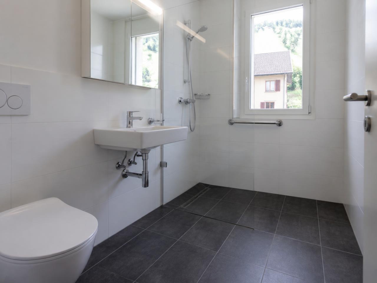 Helles Badezimmer mit bodenebener Dusche und anthrazitfarbenen Bodenfliesen